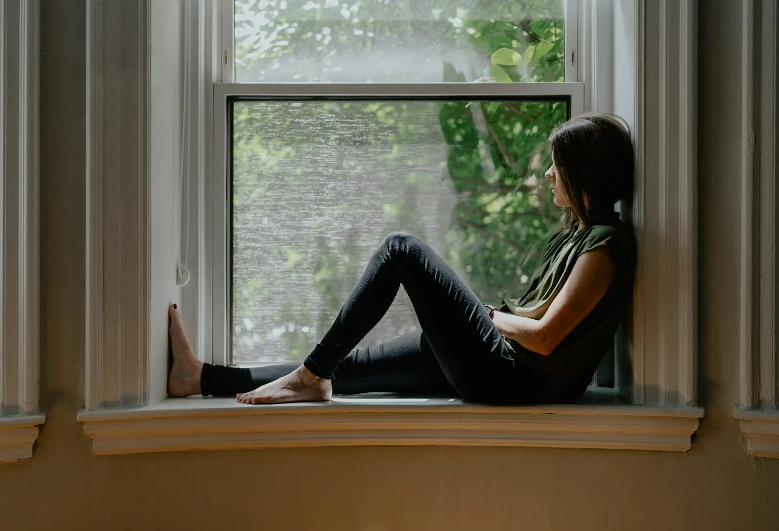 Woman sitting alone on a window sill, gazing outside