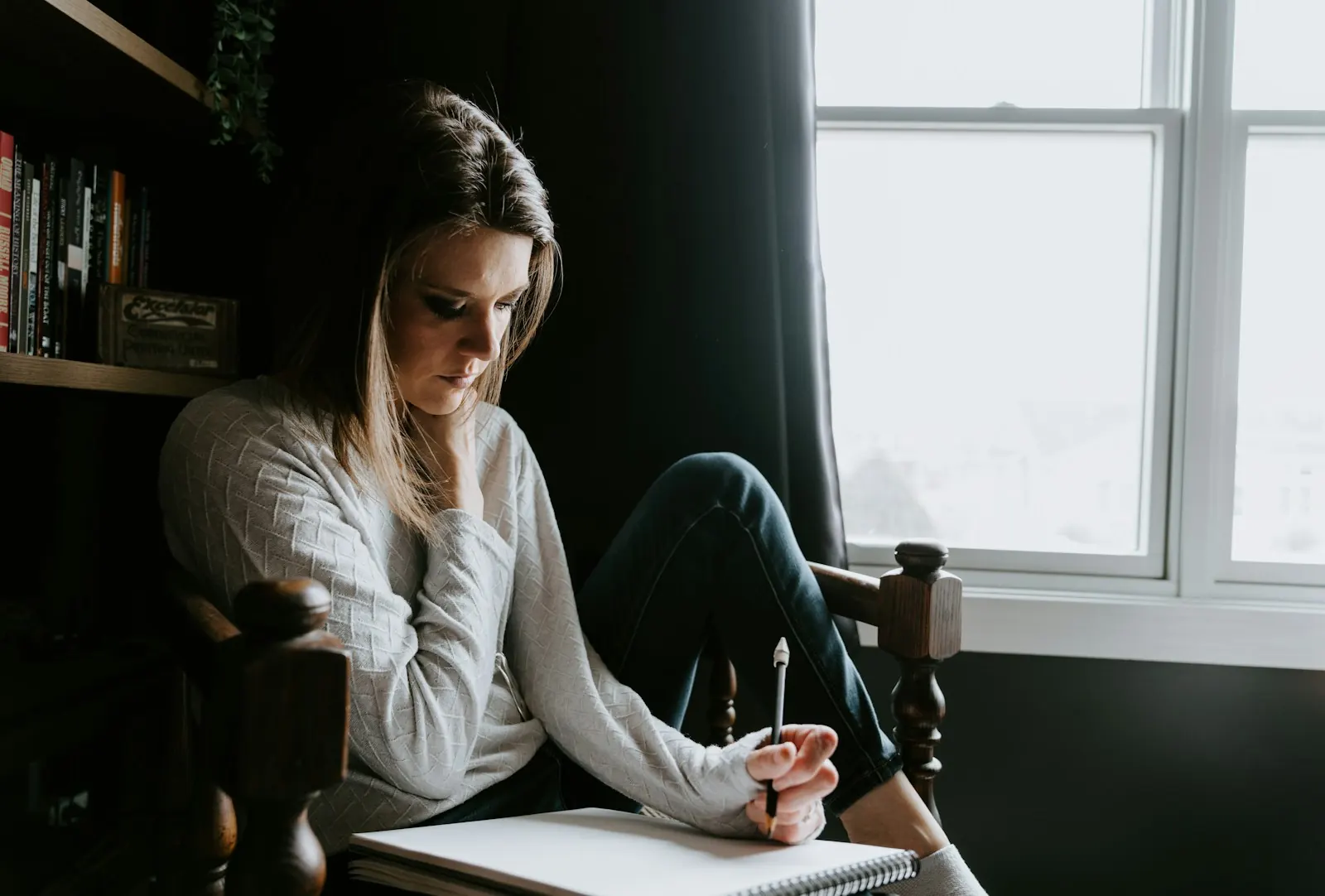 Woman sitting by a window writing in her journal