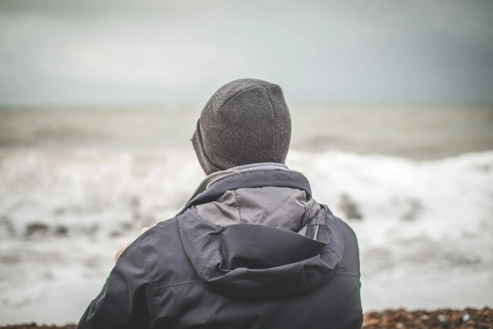 Man in a knit cap looking out at the rough sea