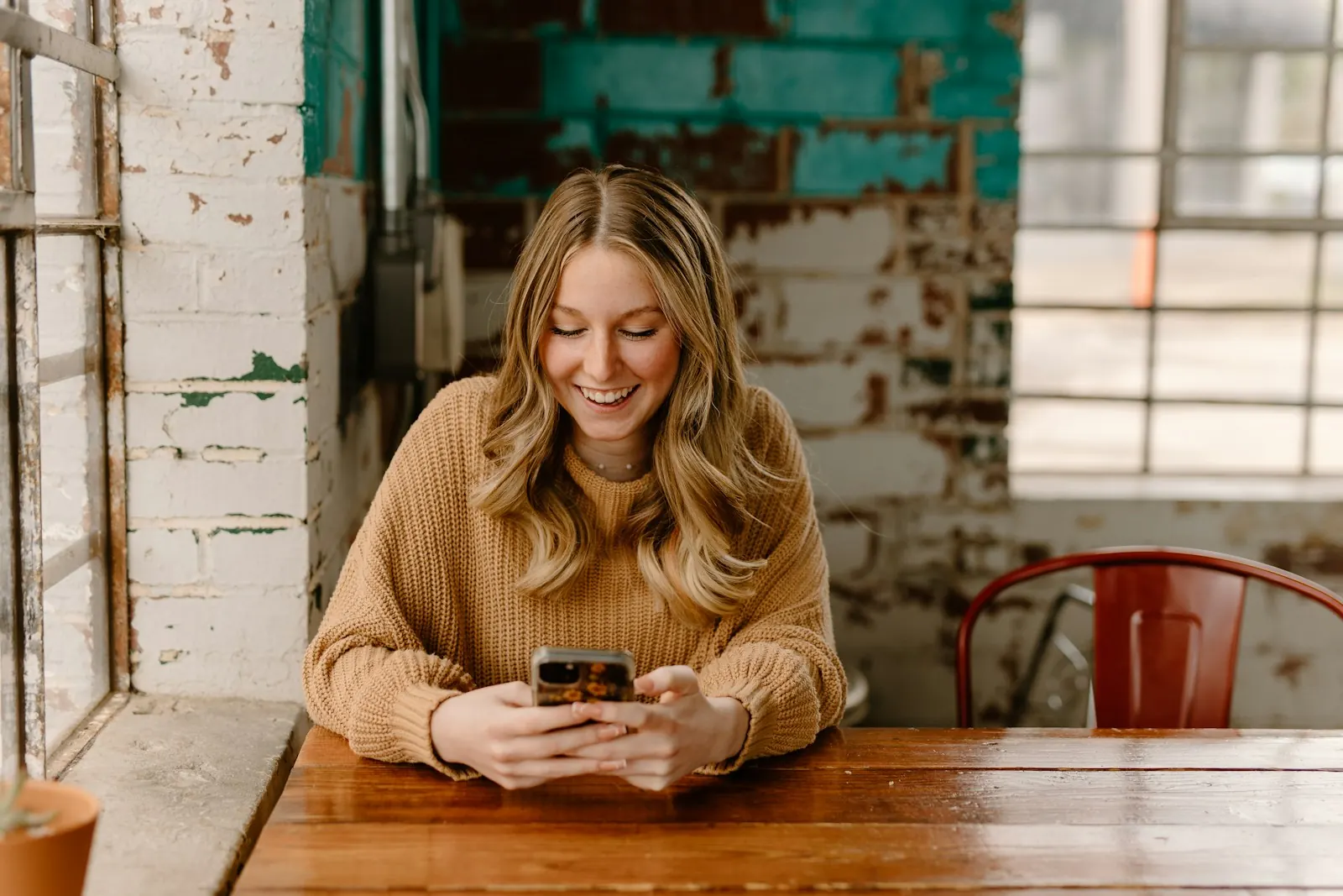 Smiling woman texting on her phone at a cafe table