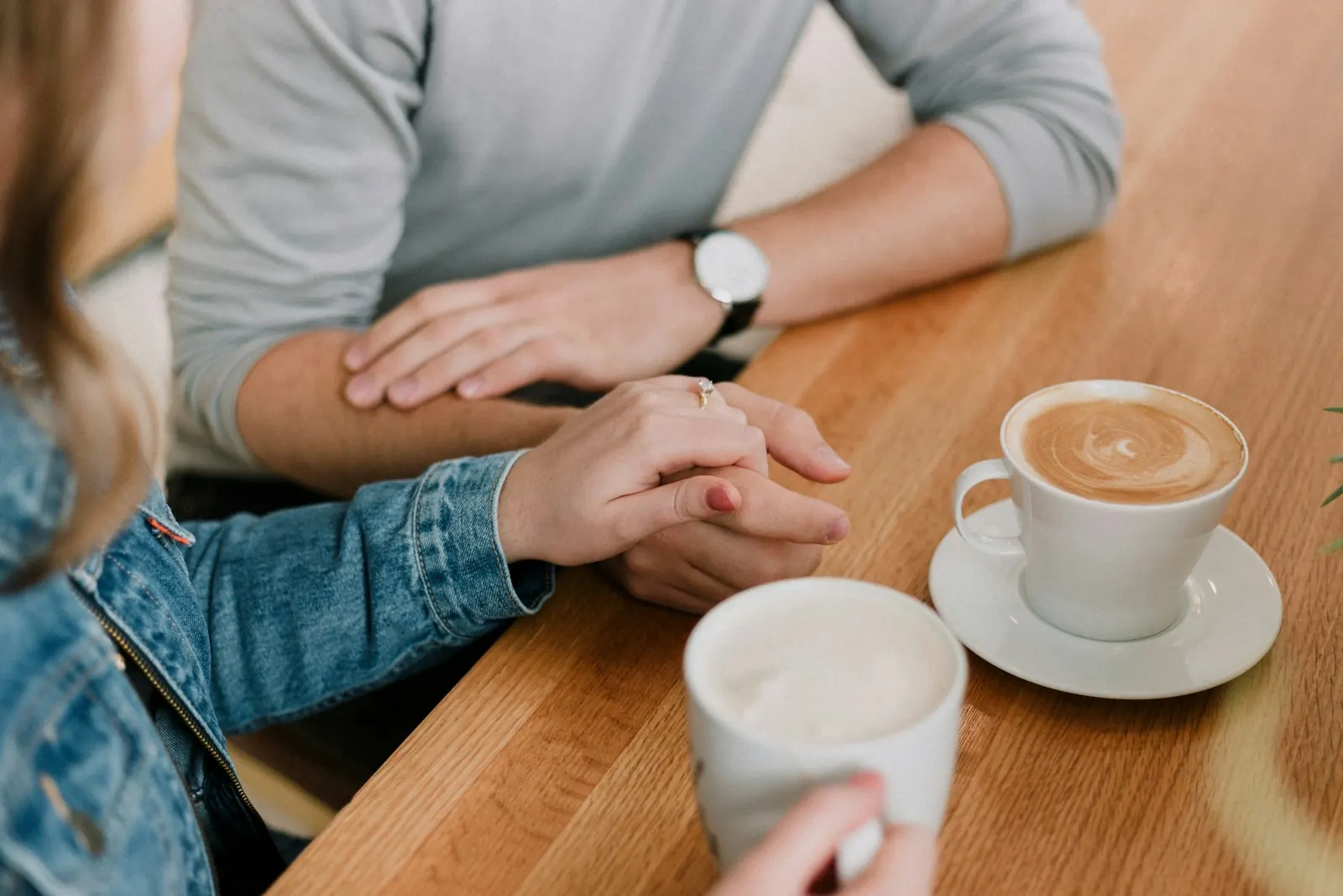 Couple holding hands across a cafe table beside cups of coffee