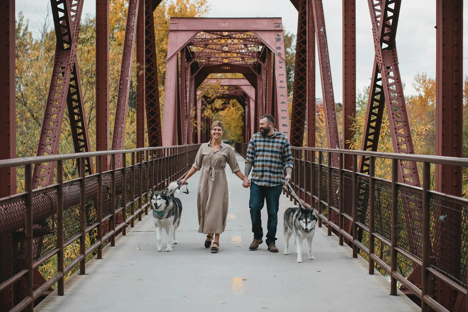 Couple holding hands while walking their dogs across a bridge