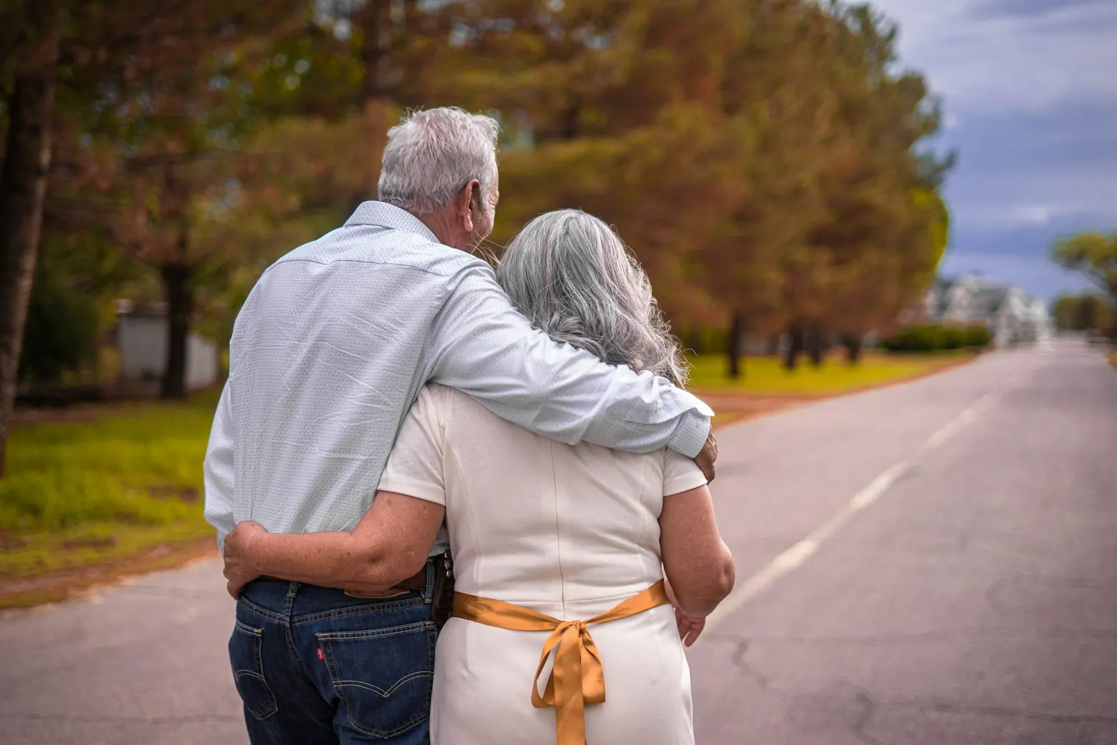 Older married couple walking arm in arm down a road
