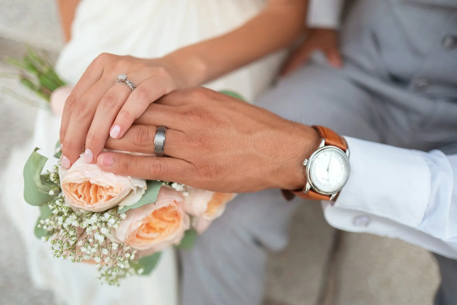 Newlywed couple's hands with wedding rings over a bouquet