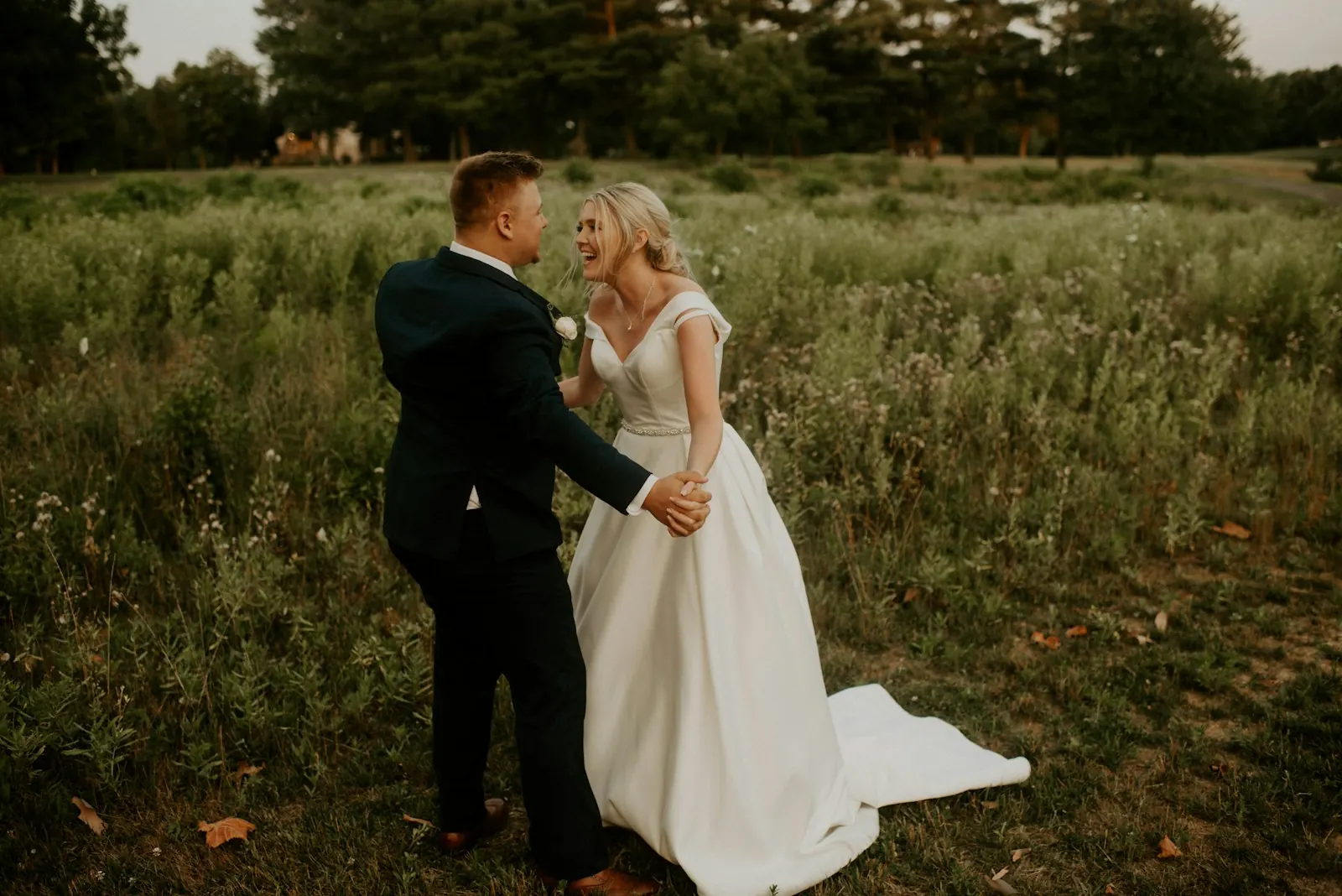 Bride and groom laughing together in a grassy field
