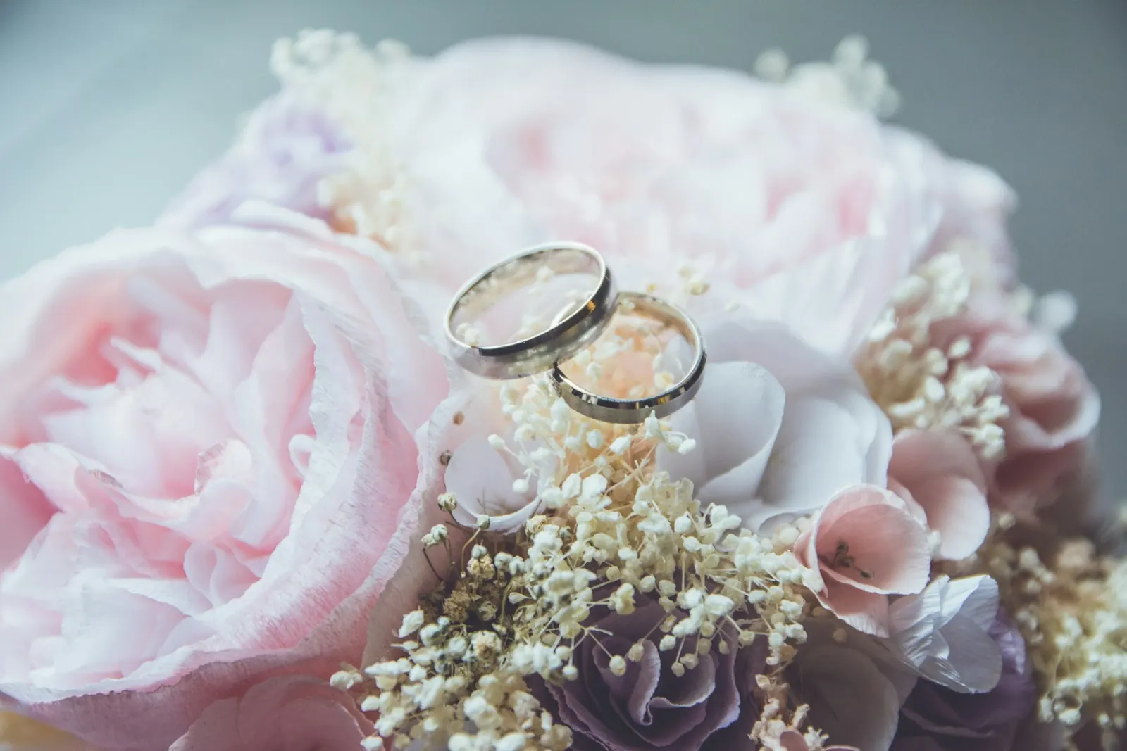 Close-up of wedding rings resting on a pink rose bouquet