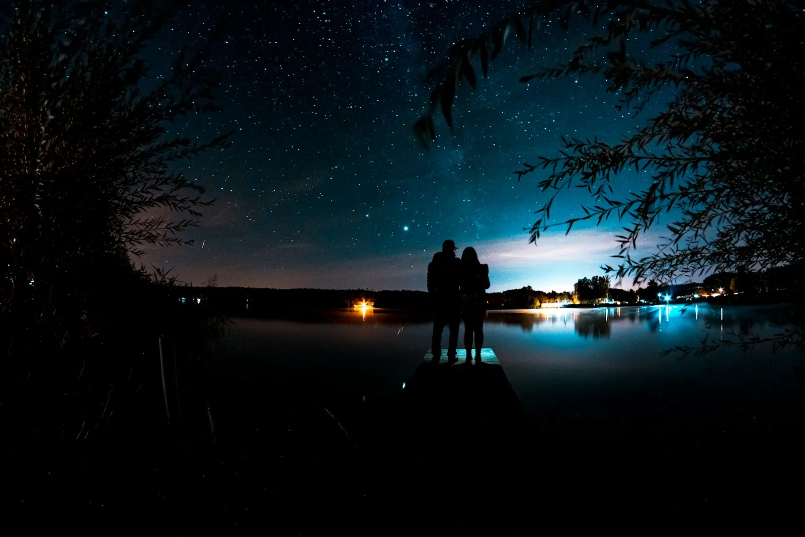 Couple silhouetted on a dock under a starry night sky