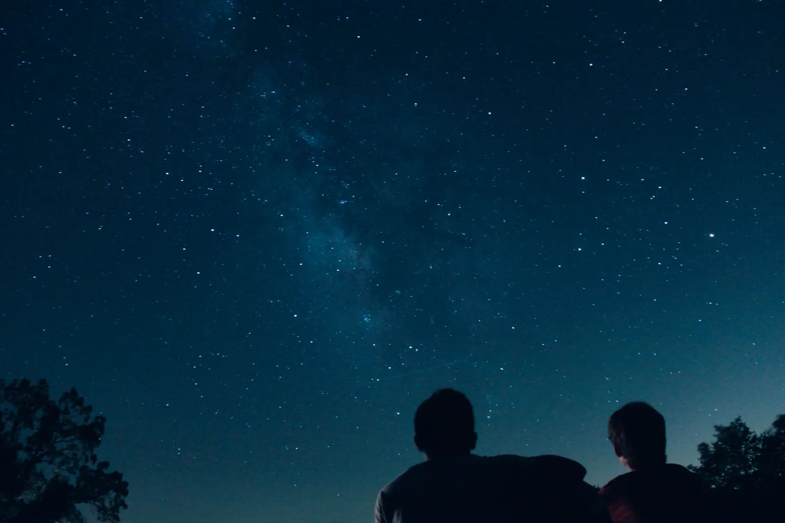 Two people stargazing on a hill under the Milky Way