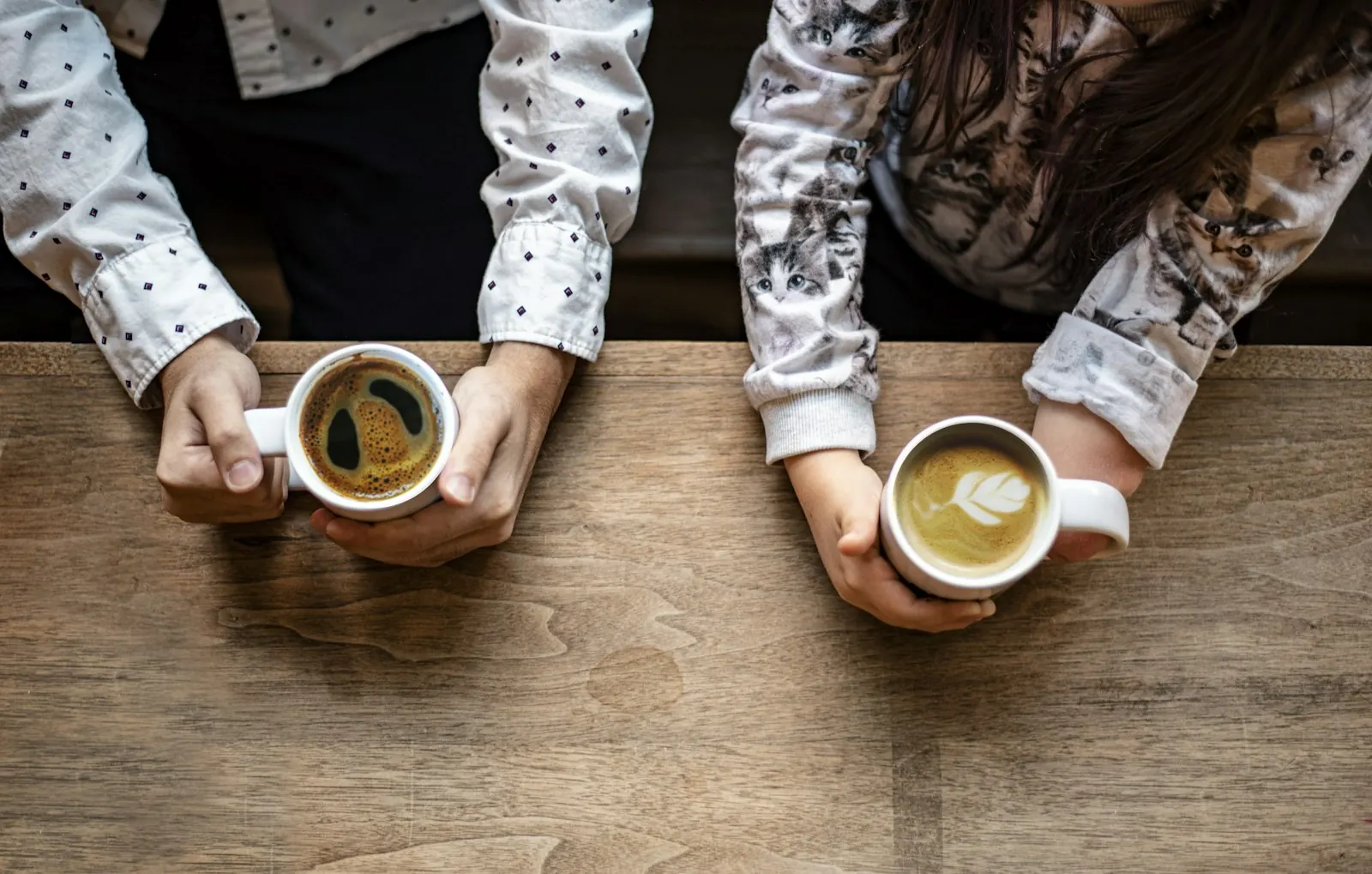 Two people holding cups of coffee on a wooden table